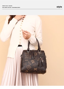 Detail of dark brown tote bag featuring letter monogram, tassel, and cat charm detail