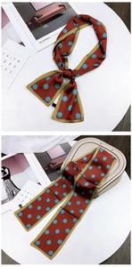 Close-up of skinny red silk scarf with blue polka dots tied on a handbag handle