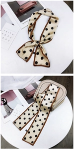 Close-up of a French polka dot skinny scarf wrapped on a beige saddle bag handle