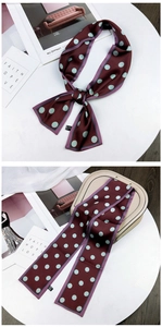Detail of wine red polka dot silk scarf tied on a beige handbag with stylish props