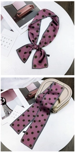 Close-up of pink polka dot silk scarf tied on a beige handbag handle for stylish accent