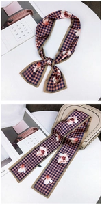 Detail of floral and houndstooth pattern silk twilly scarf tied on a beige leather handbag