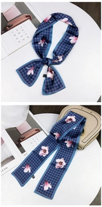 Detail of blue houndstooth floral twilly scarf styled on a beige leather handbag