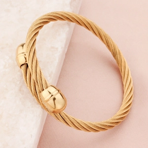 Golden twisted cable wire bracelet with polished sphere ends on a luxury marble surface