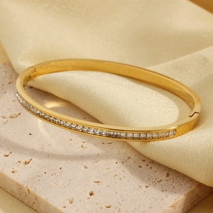 Elegant gold bangle featuring a single row of square clear zircons on a silk background