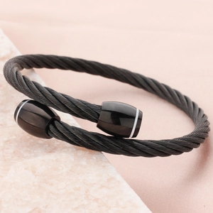 Matte black stainless steel cable cuff bracelet with striped end caps on white marble stone