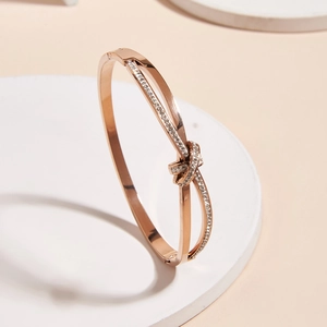 Rose gold knot bangle with sparkling rhinestones on minimalist white display stands
