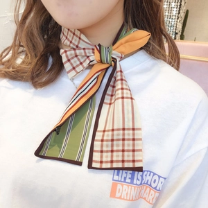 Detail of a geometric plaid silk twilly scarf with orange and green patterns on a model