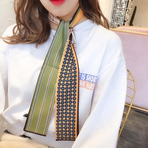 Detail of a double-sided long narrow silk scarf tied around the neck with warm lighting