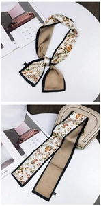 Detailed close-up of floral twilly silk scarf tied on a beige handbag with soft lighting