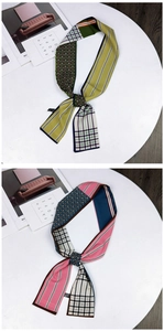 Detailed view of green and blue patterned silk twilly scarves on a white display stand