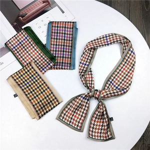 Detail of assorted houndstooth pattern silk twilly scarves on a minimalist white surface