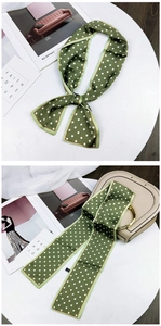 Close-up of a dark green polka dot silk twilly scarf tied on a beige handbag handle