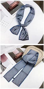 Detail of blue polka dot silk scarf with orange trim tied on table and hung on handbag