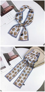 Detail of light blue twilly scarf with tiger print and red edges on a white table