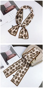 Detail of satin scarf with cartoon tiger print tied as a bow on a beige saddle bag