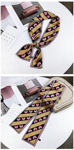 Detail of yellow and black striped silk scarf with pink hearts tied on a handbag