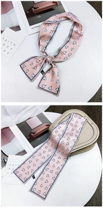 Pink heart print skinny scarf tied in a bow next to a stylish beige handbag decor