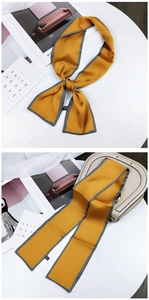 Close-up of yellow long silk scarf with geometric edges tied on a beige handbag