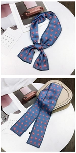 Navy blue twilly scarf with pink hearts tied on a beige saddle bag handle detail