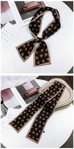 Detail of satin scarf with orange heart print and champagne trim on a stylish leather bag