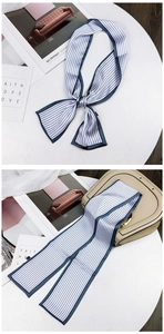 Detail of blue and white striped silk scarf tied as a bow on a luxury handbag strap