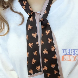 Détail d'un foulard en soie marron à motif cœur noué sur le cou d'un mannequin