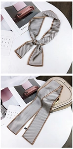 Close-up of champagne silk twilly scarf with black stripes on a stylish handbag