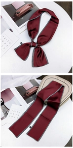 Close-up of wine red silk scarf with black and white striped edges on a white podium