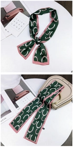 Detail of dark green twilly scarf with pink horseshoe pattern tied on a handbag