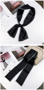 Detail of black silk twilly scarf with white edge tied on a stylish beige handbag