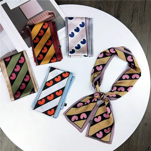 Five assorted skinny silk scarves with heart and stripe patterns on a white table