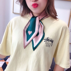 Detail of pink and dark green silk scarf tied around neck featuring heart pattern