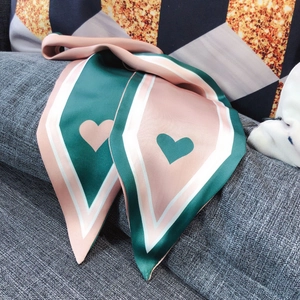 Macro shot of pink and dark green silk scarf with heart patterns on grey fabric