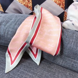 Detail of a silky long scarf with pink base and green accents on a textured sofa