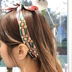 Detailed view of a pink and green plaid satin scarf tied as a hair bow accessory