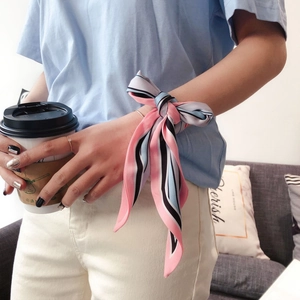 Close-up of a striped silk scarf worn as a stylish wrist accessory holding a cup