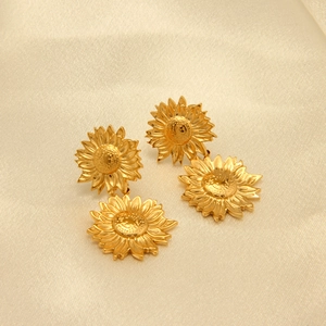 Dettaglio di orecchini a goccia girasole dorati su elegante tessuto di raso beige