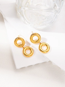 Close-up of shiny gold double hoop drop earrings on white textured stone background