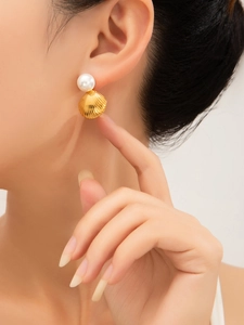 Close-up of elegant pearl and gold shell earrings worn on ear with ocean-inspired design