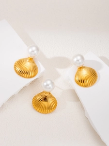 Detail view of gold shell earrings with white pearls on a minimalist stone display