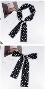 Détail d'un foulard en soie à pois noirs et blancs avec bordure contrastée noué en deux nœuds chics
