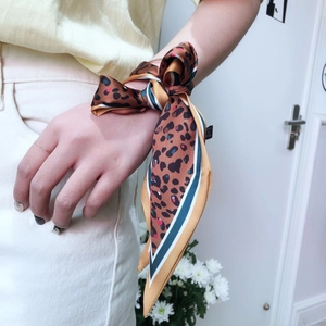 Close-up of leopard print skinny silk scarf tied in a bow on wrist with green accents