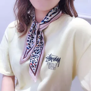 Close-up of leopard print skinny silk scarf tied as a neck bow in beige and blue