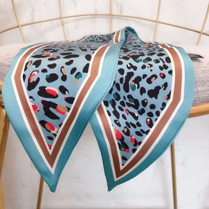Detail of blue leopard print silk scarf draped on golden chair with marble background