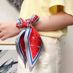 Detail of red silk scarf with dog print and polka dots tied as a wrist bow