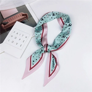 Detail of mint green twilly scarf with dog print and contrast borders on a white surface