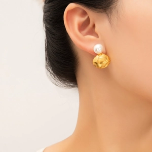 Elegant gold shell earrings with white pearl detail worn on a model for ocean-inspired style