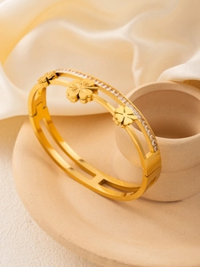 Detail of 18k gold plated clover bangle with zircon stones on a beige ceramic tray