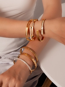 Detailansicht gestapelter goldener Titanstahl-Armbänder mit Zirkonia und Nageldesign